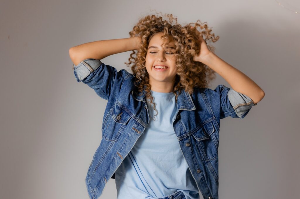 portrait of a young happy woman adjusting her blonde curly hair with her hands. hair products