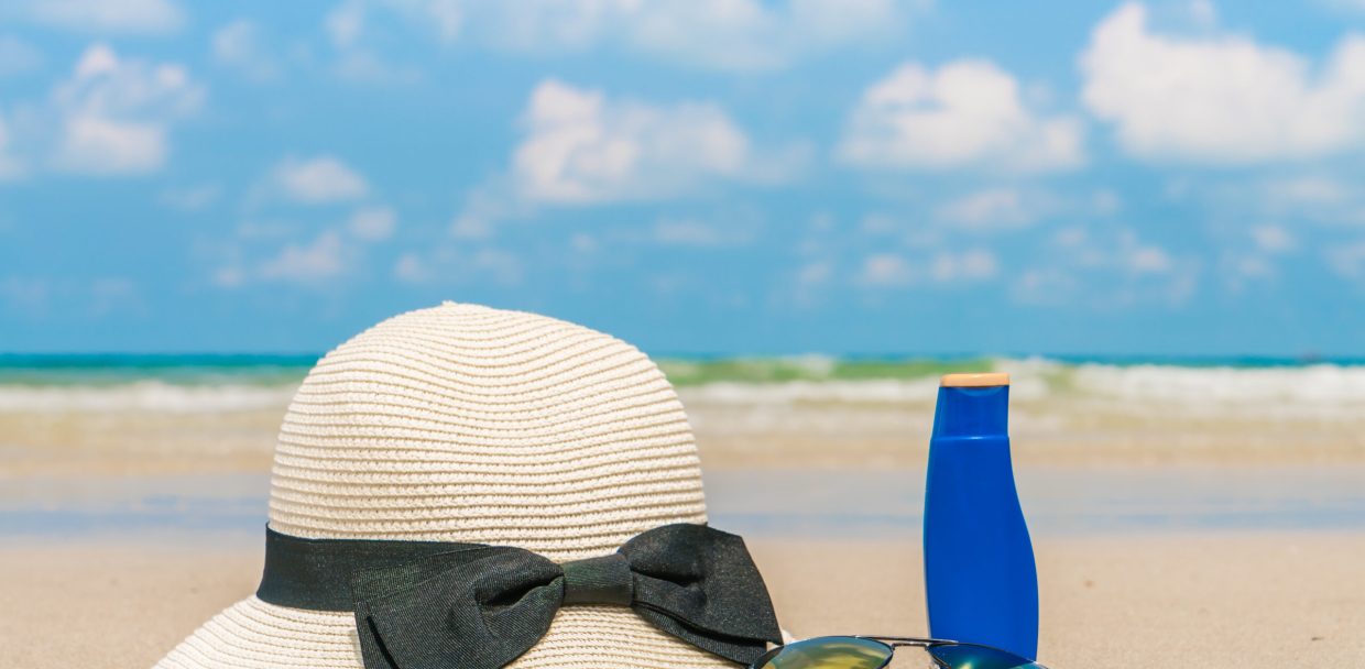 Sunglasses, sun cream and hat  on white  sand beach